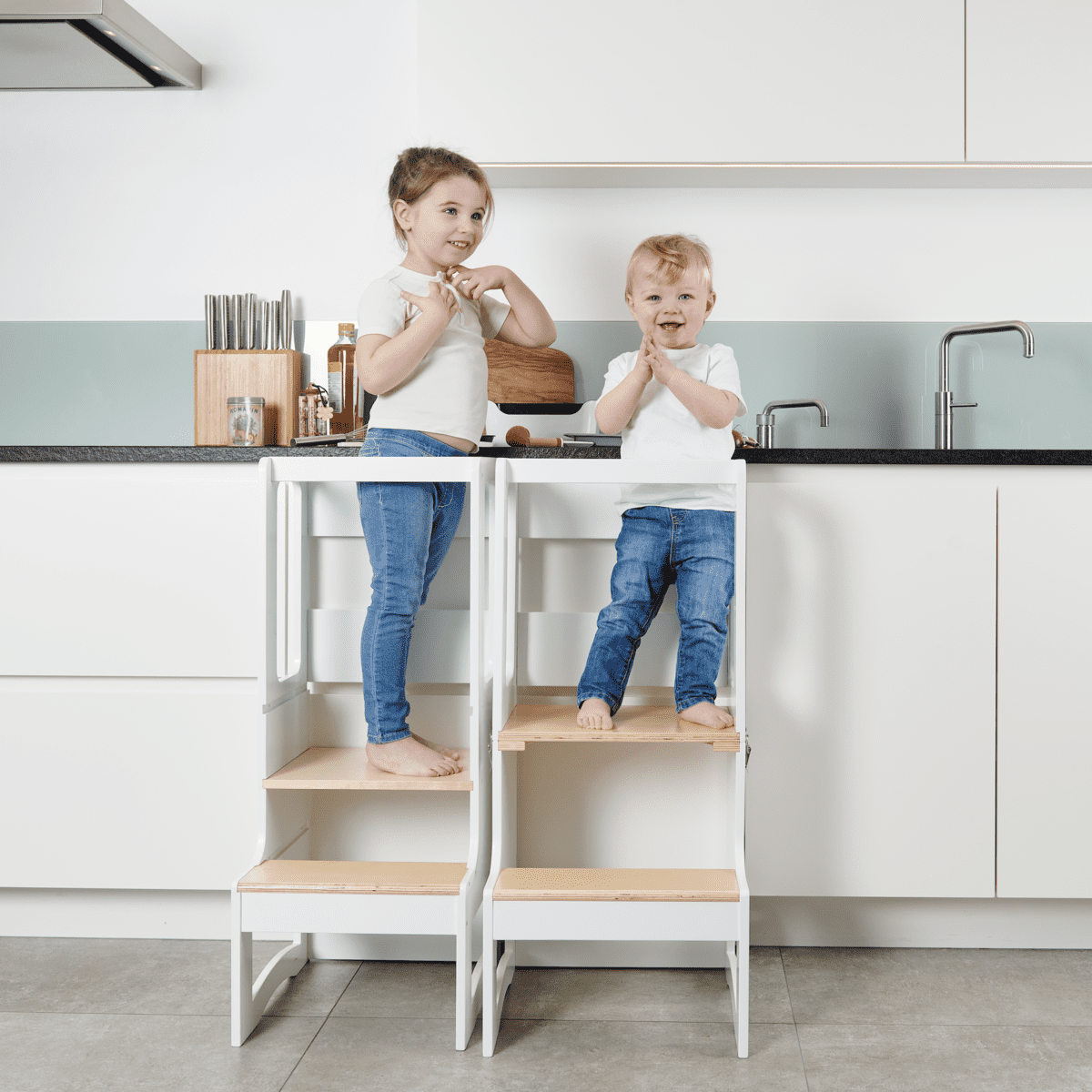 een kleuter en een peuter staan op een leertoren in de keuken